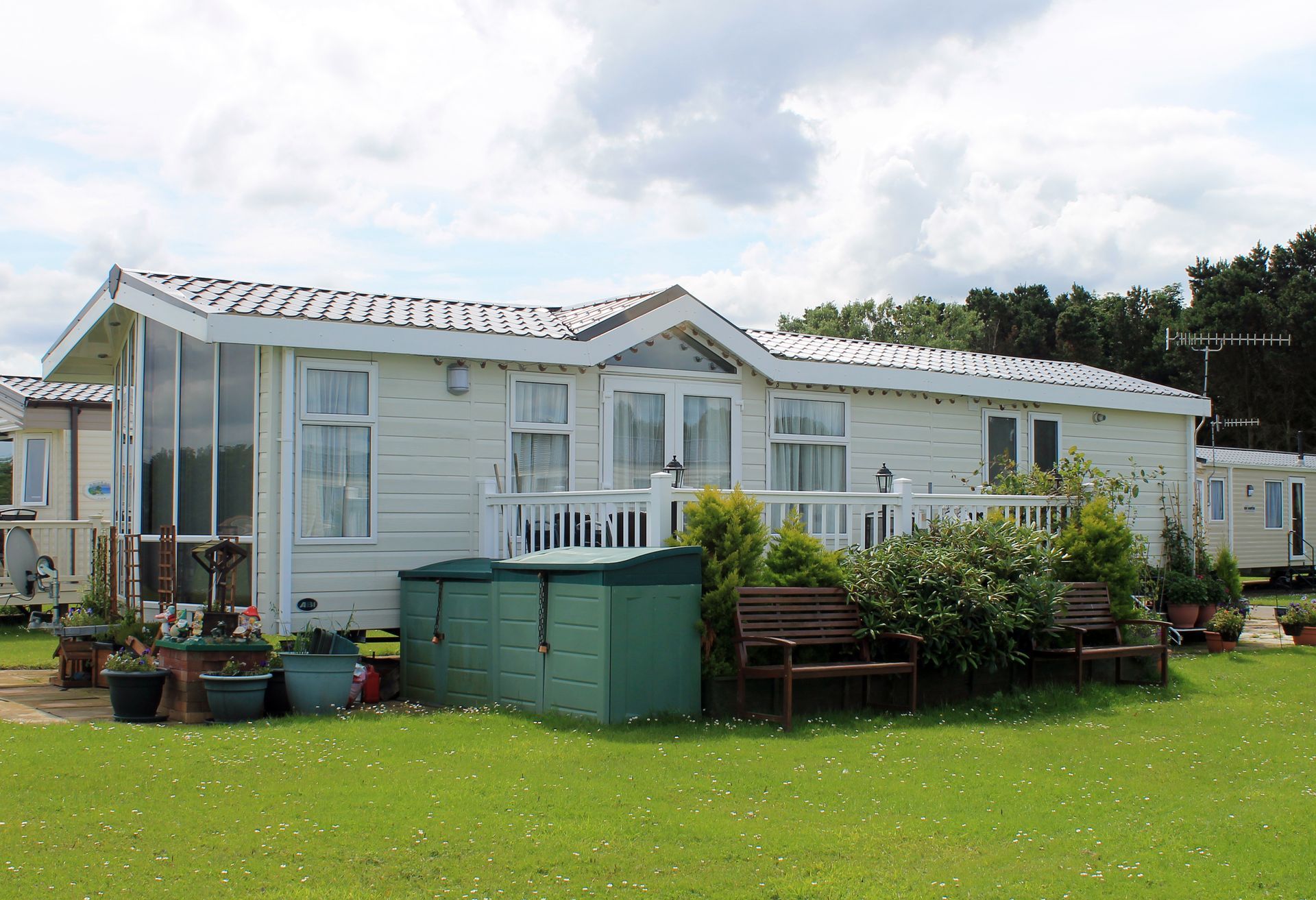 A cream-colored manufactured home with pitched roof, white deck railings, landscaped yard, blue sky
