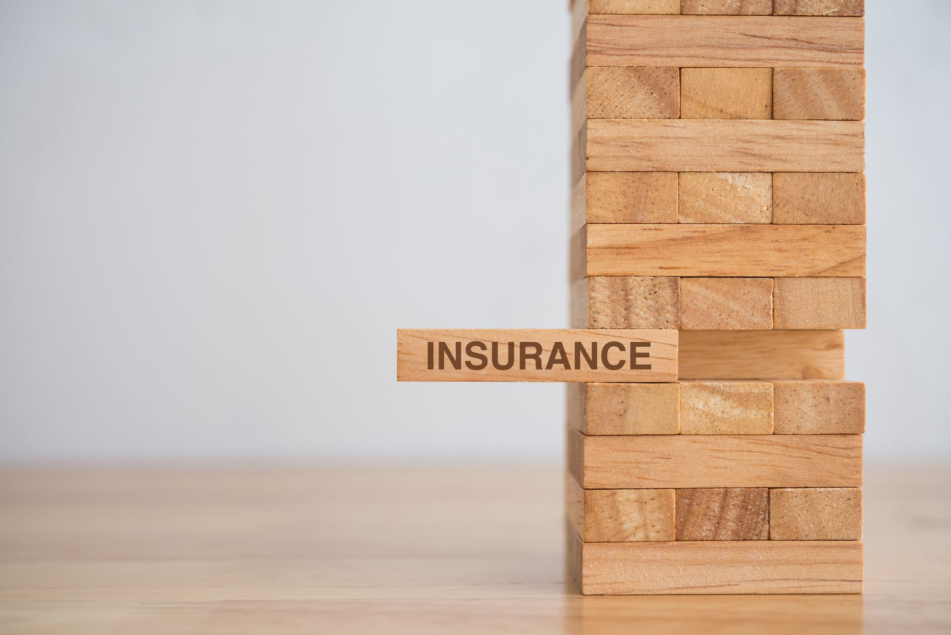Wooden block labeled “Insurance” being pulled from a stacked tower of blocks.