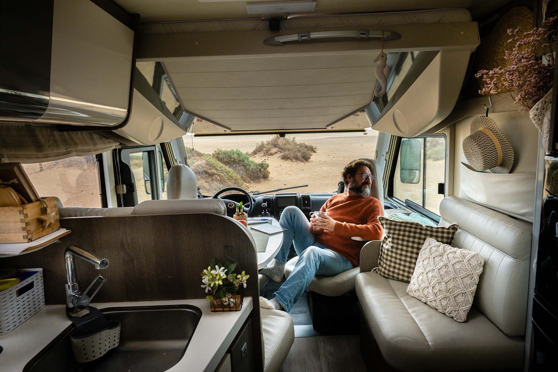 Interior of a camper van with seating, kitchenette, and wide front view overlooking a landscape. Interior of a camper van with seating, kitchenette, and wide front view overlooking a landscape.