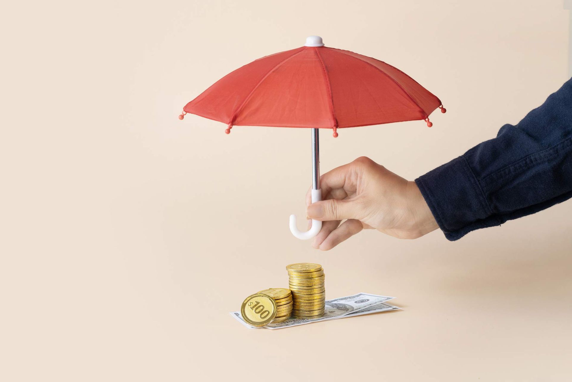 Hand holding a red umbrella over a stack of coins and notes.