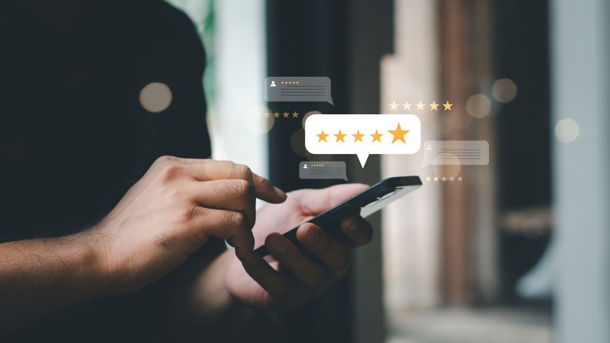Person using a smartphone to view online reviews, with five-star rating and speech bubbles in the background.