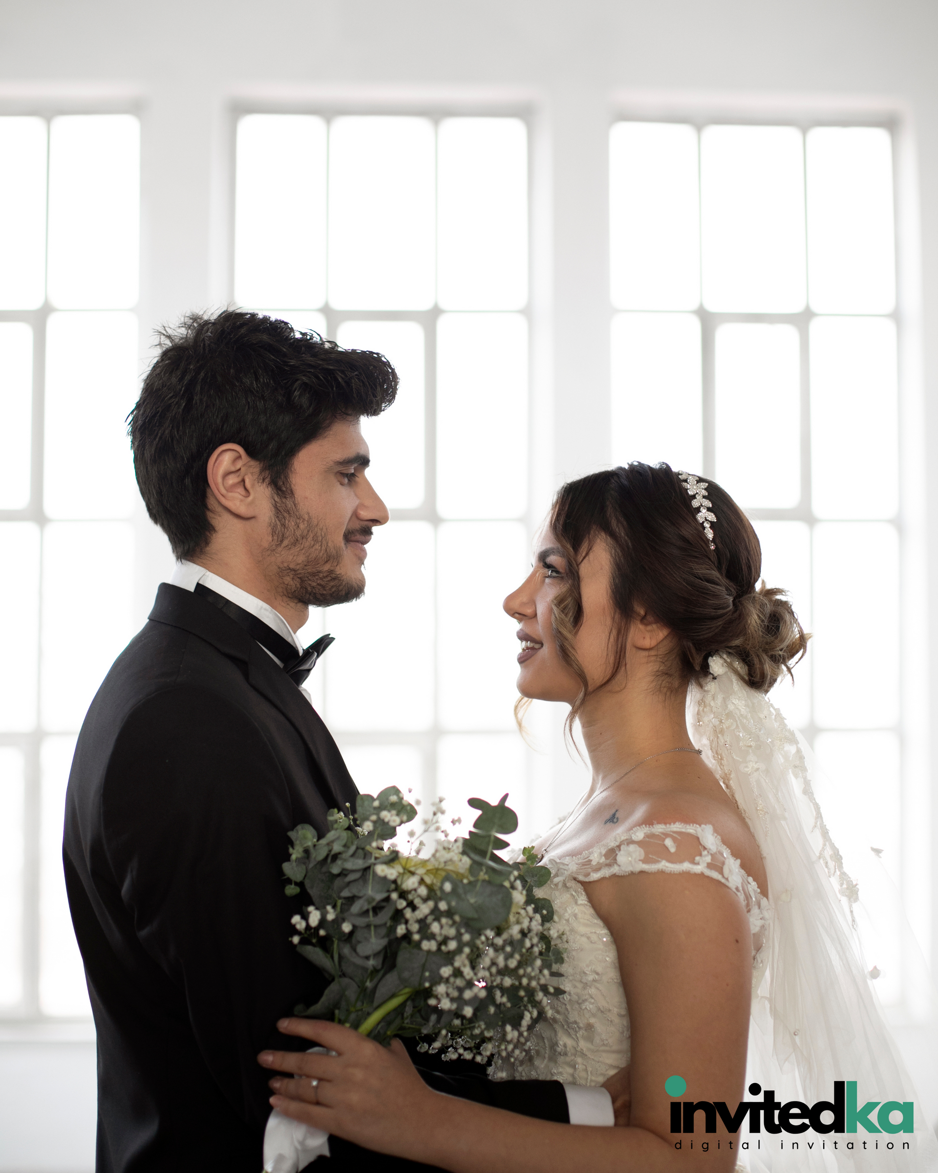 A bride and groom are looking at each other in front of a window.
