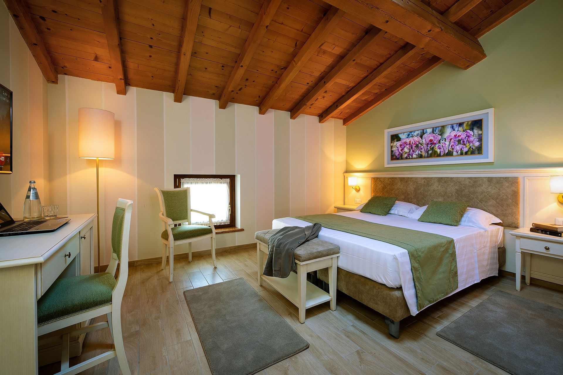 Accogliente camera da letto con soffitto in legno, letto matrimoniale, poltrona e lampade a luce calda vicino a una finestra luminosa.