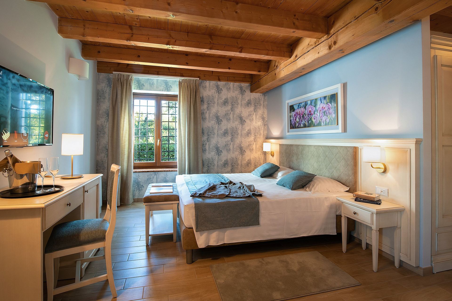 Accogliente camera da letto con travi in ​​legno a vista, pareti blu, letto, comodino e vista dalla finestra.
