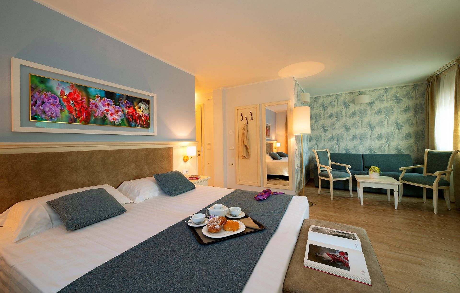 Camera d'albergo moderna con letto king size, quadri colorati alle pareti, zona salotto e luci soffuse.