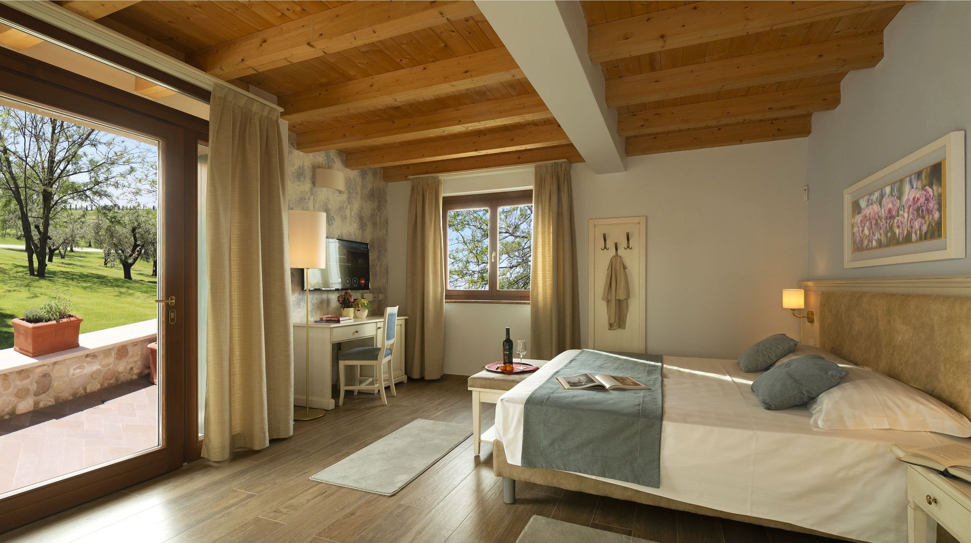 Accogliente camera da letto con soffitto con travi a vista, porte finestre che si aprono sul balcone e un letto accanto a una finestra con vista sulla campagna.