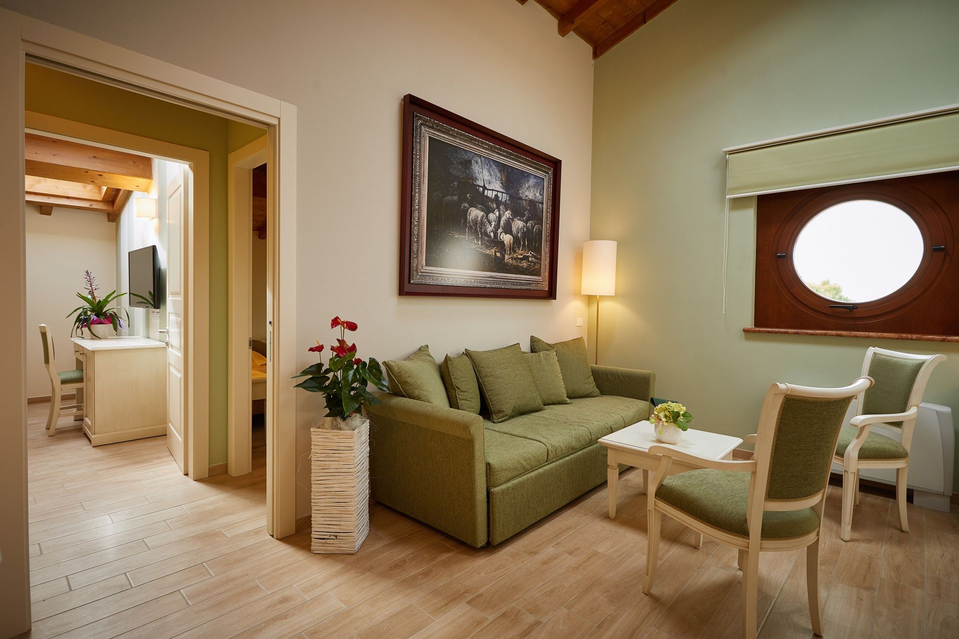 Accogliente soggiorno con divano verde, sedie, lampada, quadri alle pareti e una porta aperta che conduce al bagno.