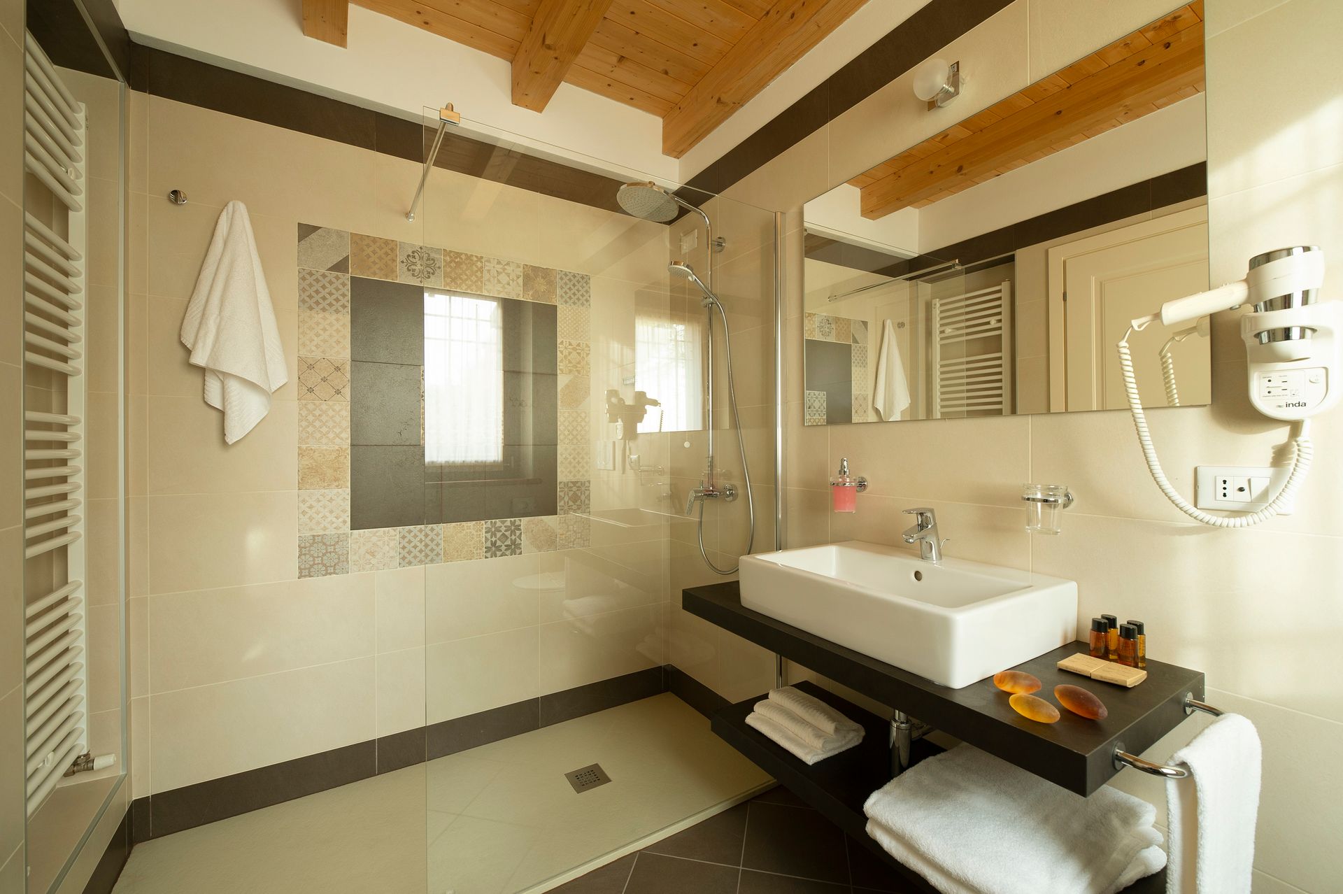 Bagno moderno di un hotel con doppio lavabo, specchio, portasciugamani e rivestimento in piastrelle beige.