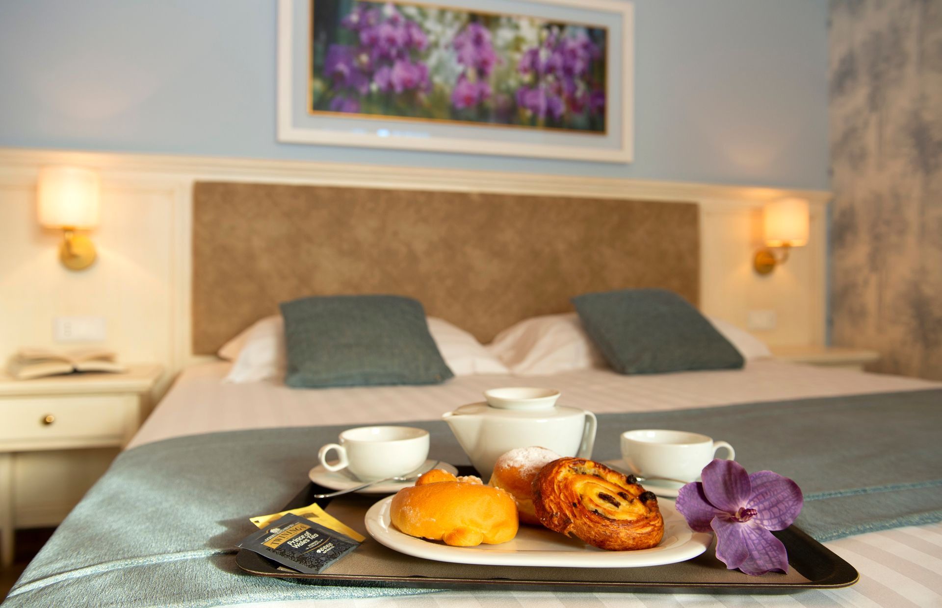 Un vassoio per la colazione sul letto in un'accogliente camera d'albergo con caffè, pasticcini e fiori viola.