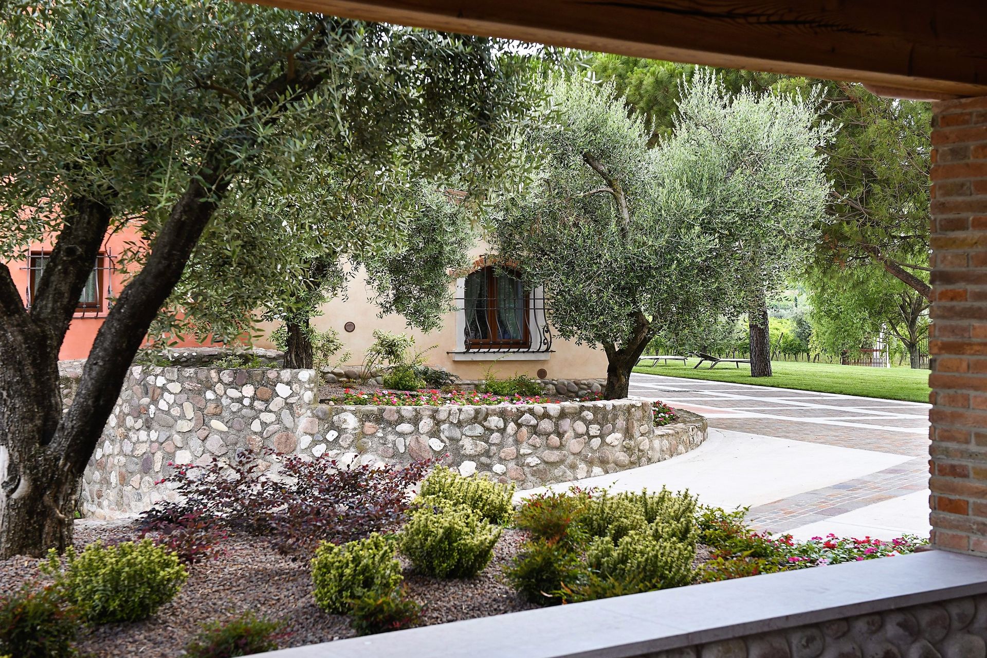 Cortile con muro di contenimento in pietra, alberi, arbusti e un vialetto pavimentato vicino a un edificio