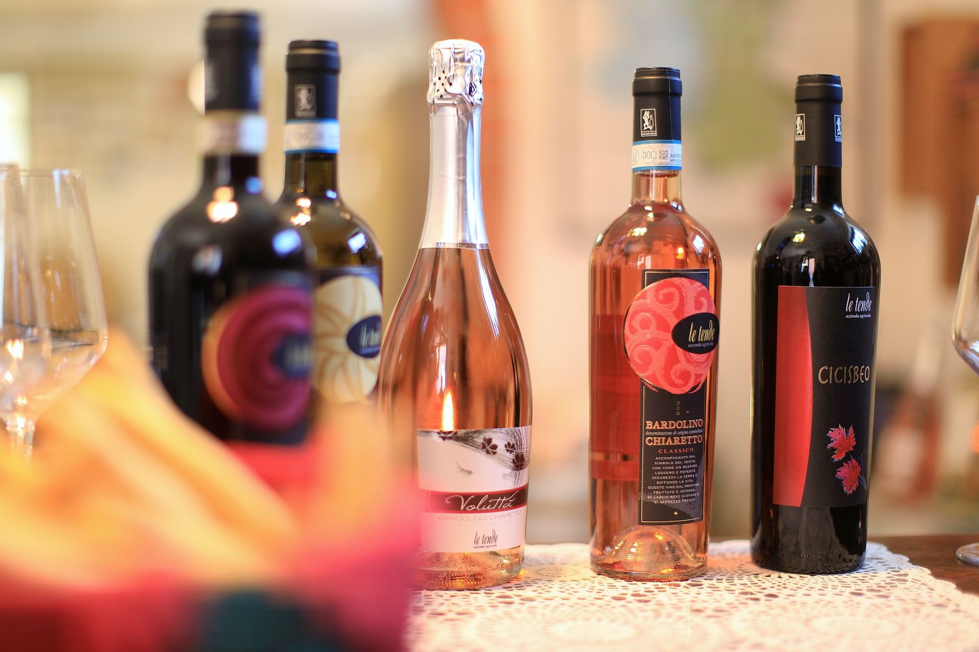 Diverse bottiglie di vino esposte su un tavolo, con bicchieri sfocati in primo piano.