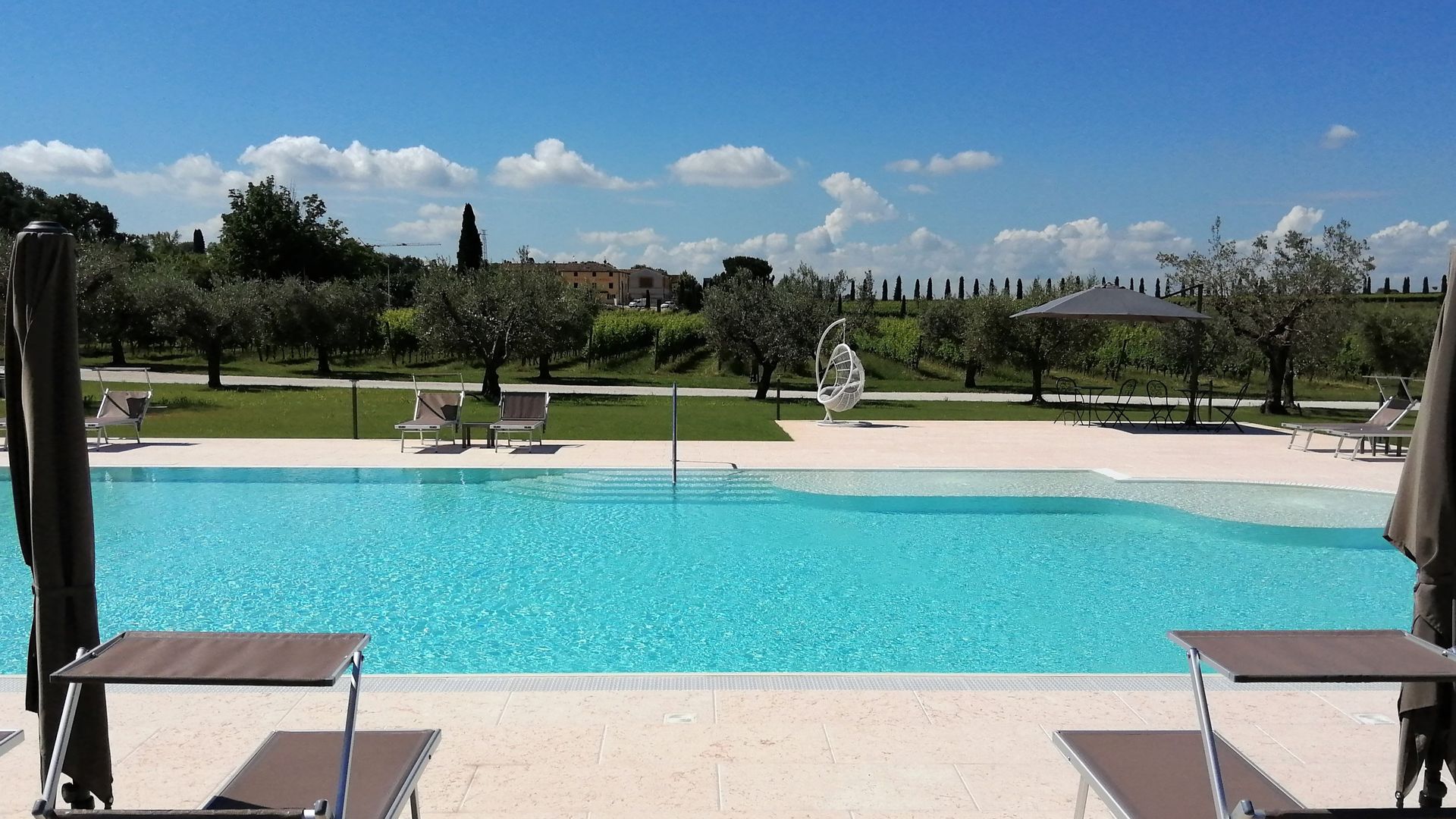 Piscina con acqua turchese, lettini prendisole e un giardino curato sotto un cielo azzurro e limpido.