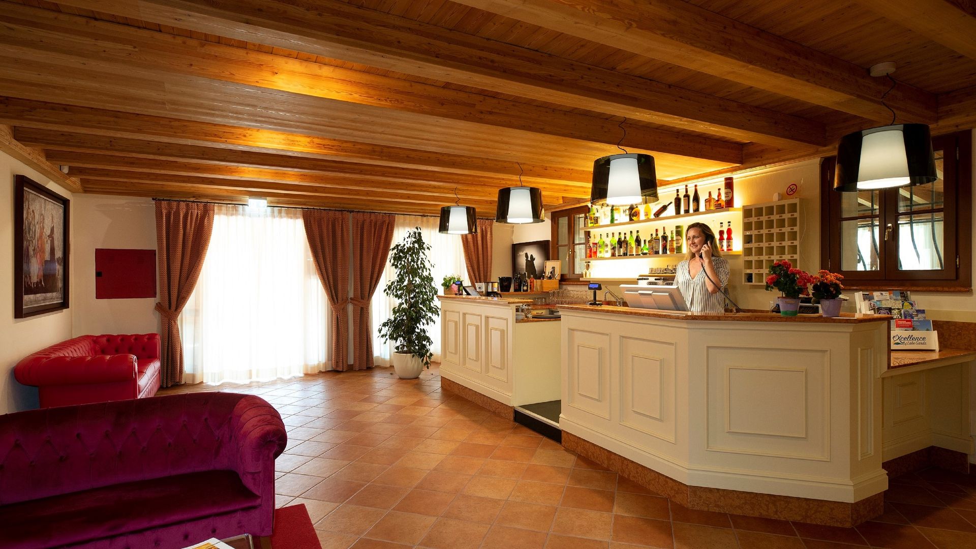 Accogliente soggiorno-cucina in stile rustico con soffitto in legno, mobili color crema, divano rosso e porta luminosa.