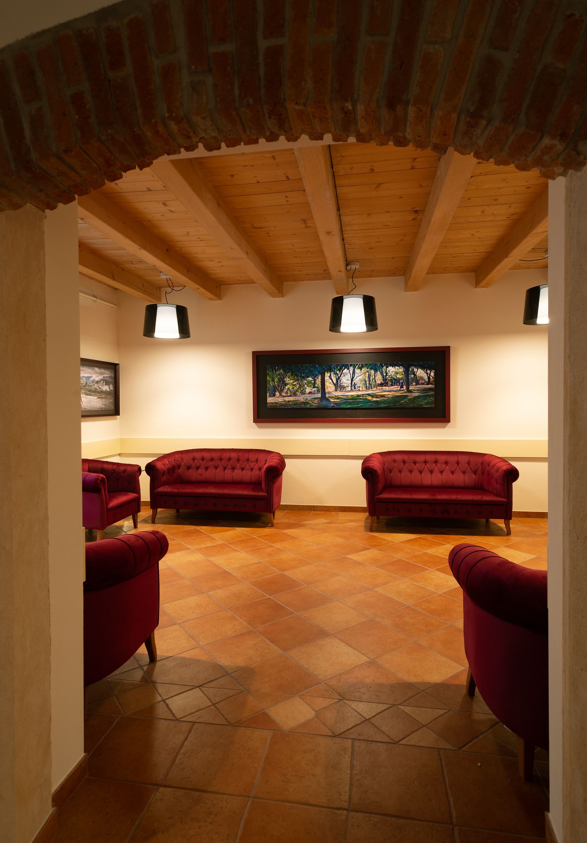Cozy lounge with red sofas, tiled floor, brick archway, and wall art.
