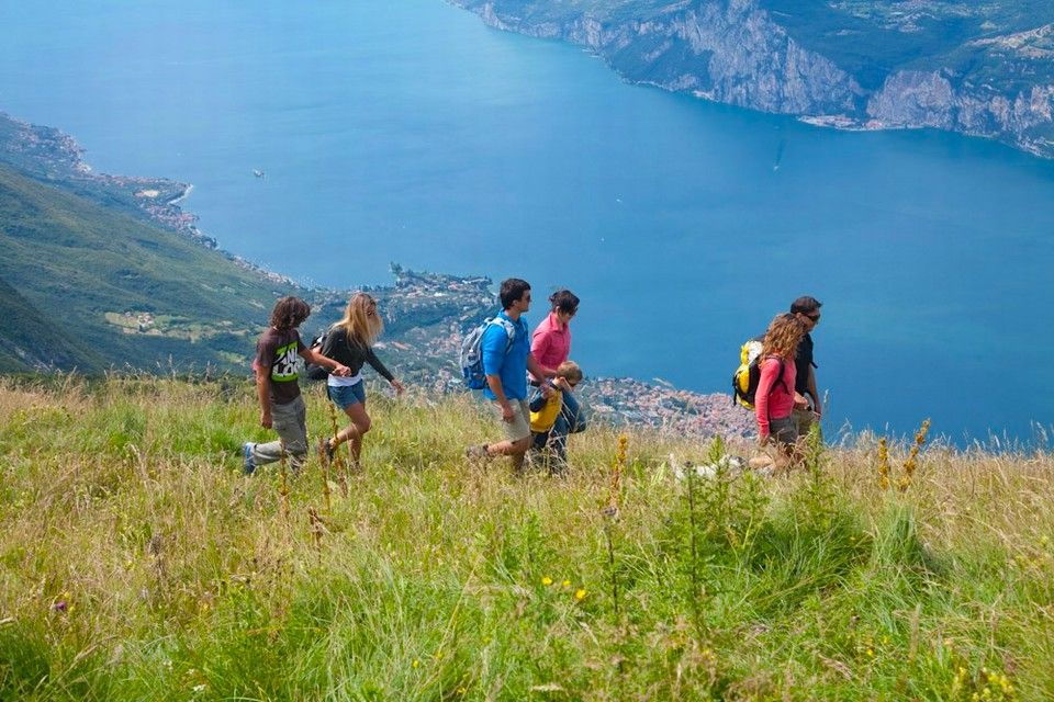 Escursionisti che camminano tra l'erba alta su un pendio che si affaccia su un lago blu e sulle scogliere.