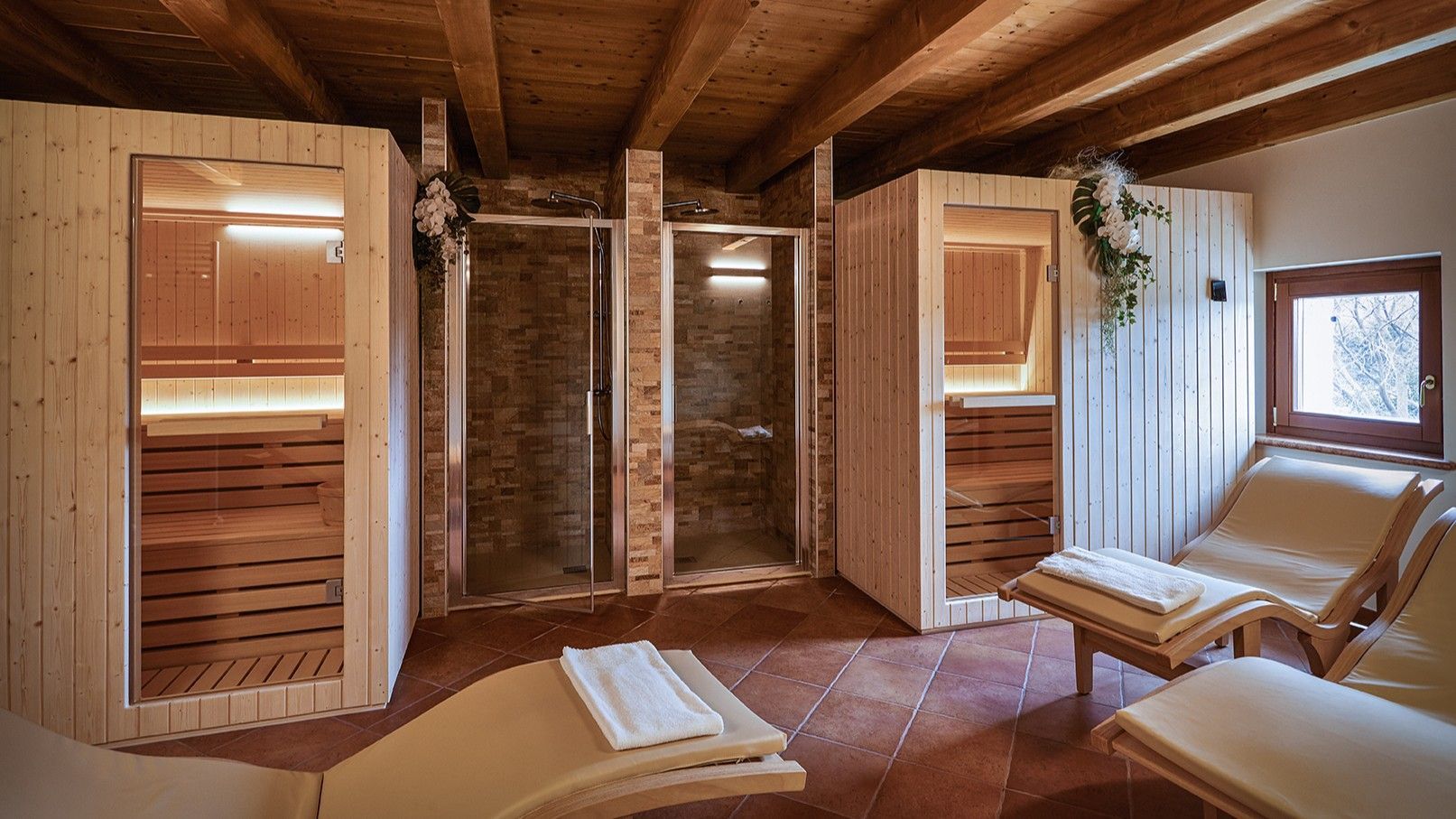 Wooden sauna with two heat rooms, glass shower, and lounge chairs in a rustic spa setting