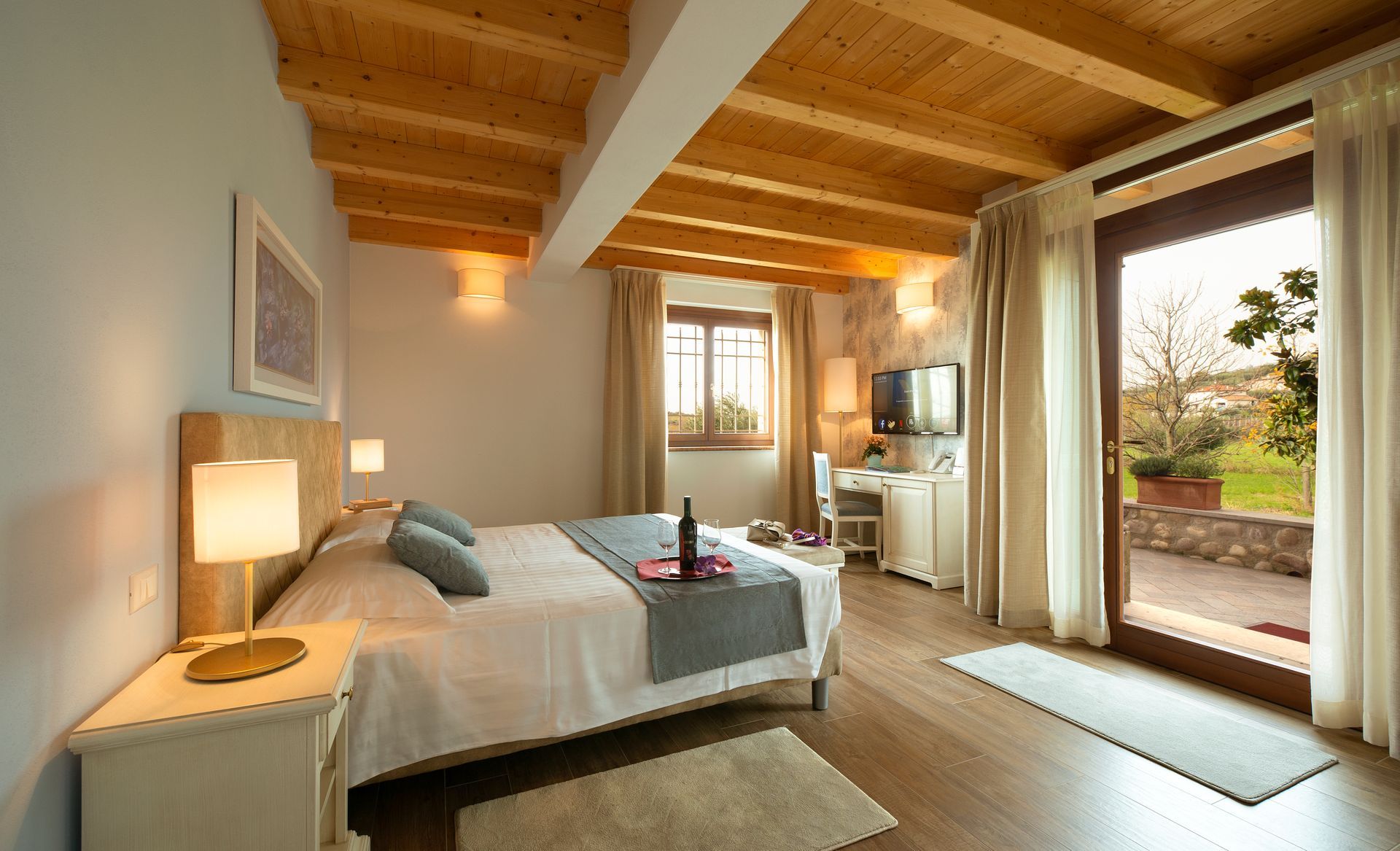 Helles, rustikales Schlafzimmer mit Holzbalken, Bett, Kommode und einer Glastür mit Blick auf die Terrasse.