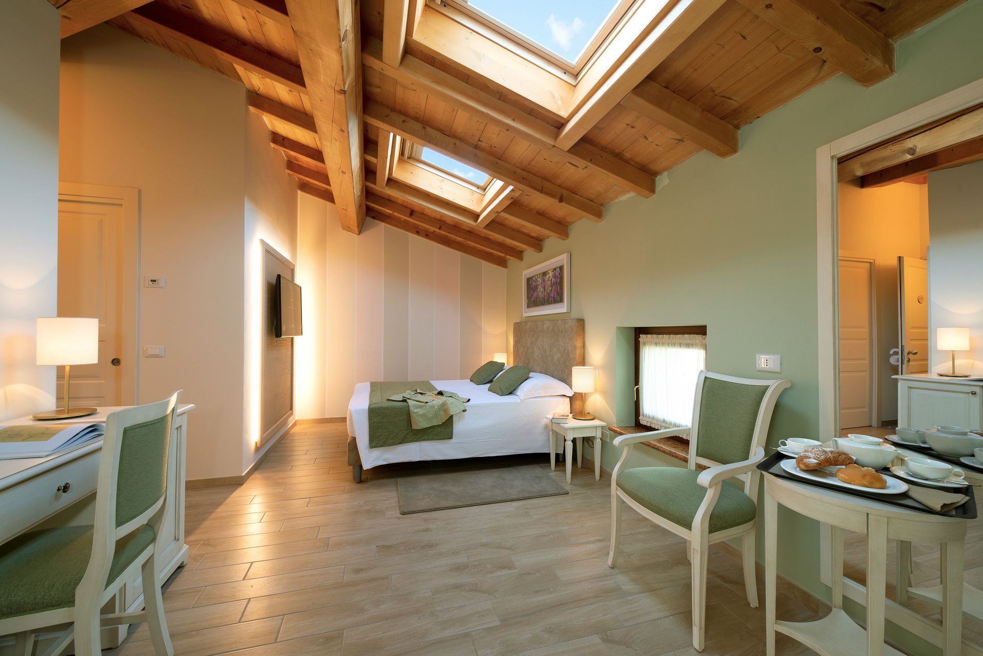 Helles Schlafzimmer mit Dachfenster, Holzbalken, hellgrünen Wänden und passenden Stühlen und Schreibtischen.