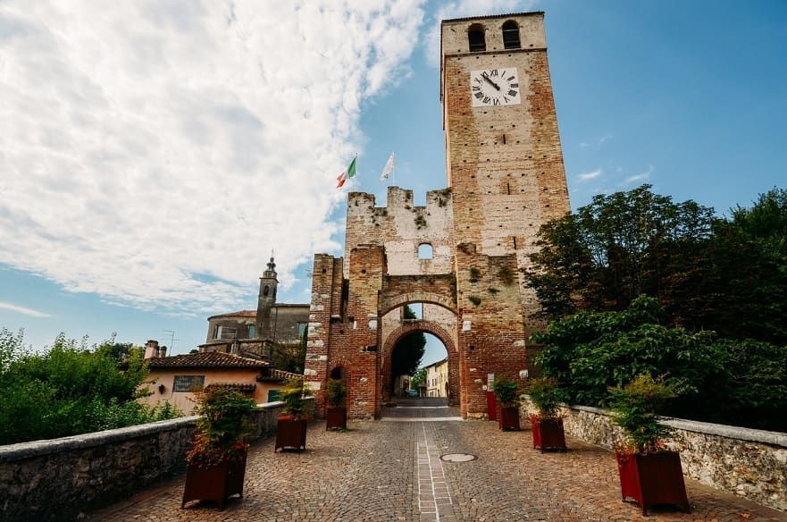 Porta del castello in pietra con torre dell'orologio e ingresso ad arco sotto un cielo nuvoloso
