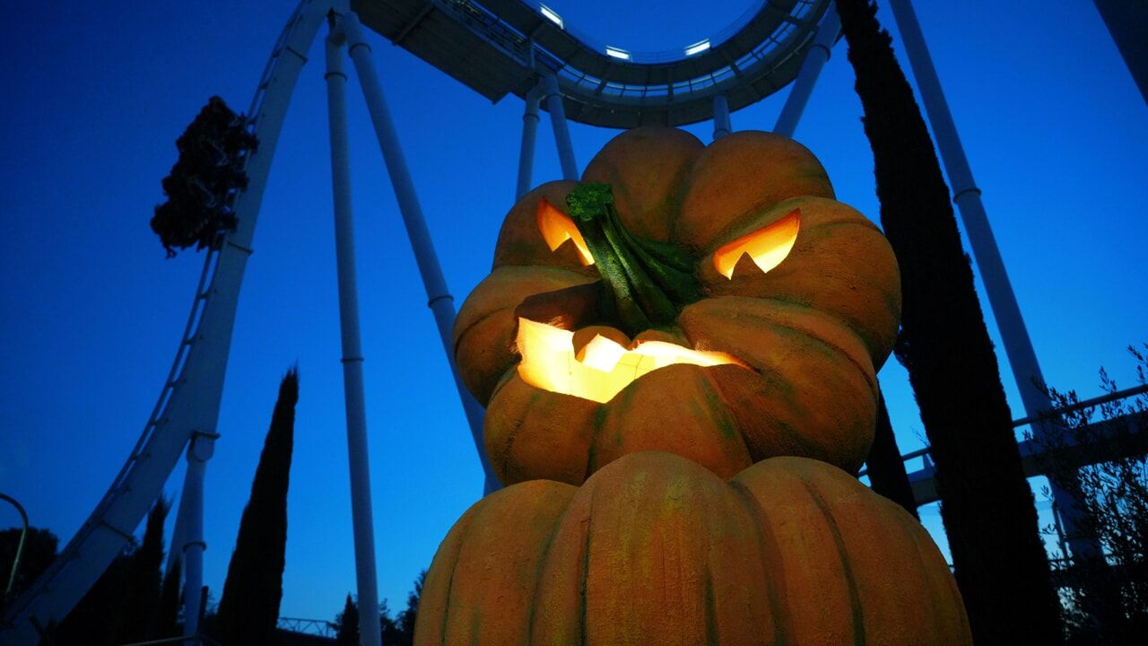 Una scultura luminosa a forma di zucca intagliata di notte, sotto la sagoma di un ottovolante.
