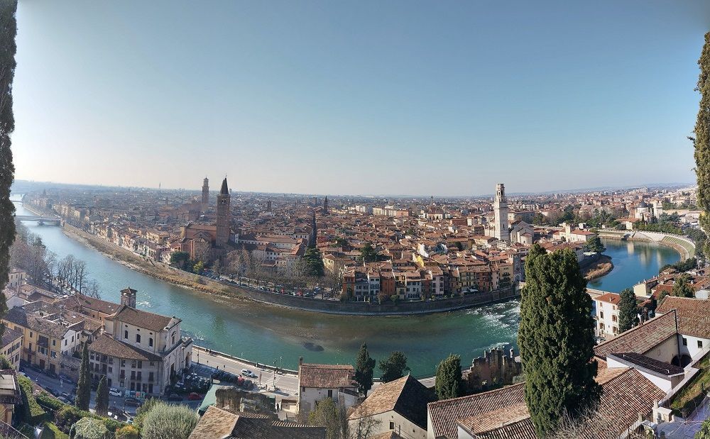Veduta panoramica del Canal Grande di Venezia, con tetti, ponti e un campanile in lontananza sotto un cielo azzurro.