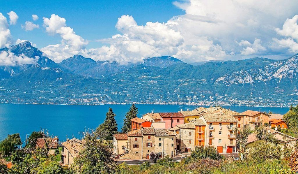 Villaggio lacustre con tetti di terracotta e montagne sotto un cielo azzurro brillante