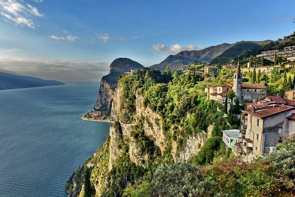 Villaggio a picco sul mare, sotto un cielo soleggiato, con scogliere rocciose e una vegetazione lussureggiante.