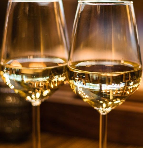 Two glasses of white wine on a bar counter, softly lit in warm tones
