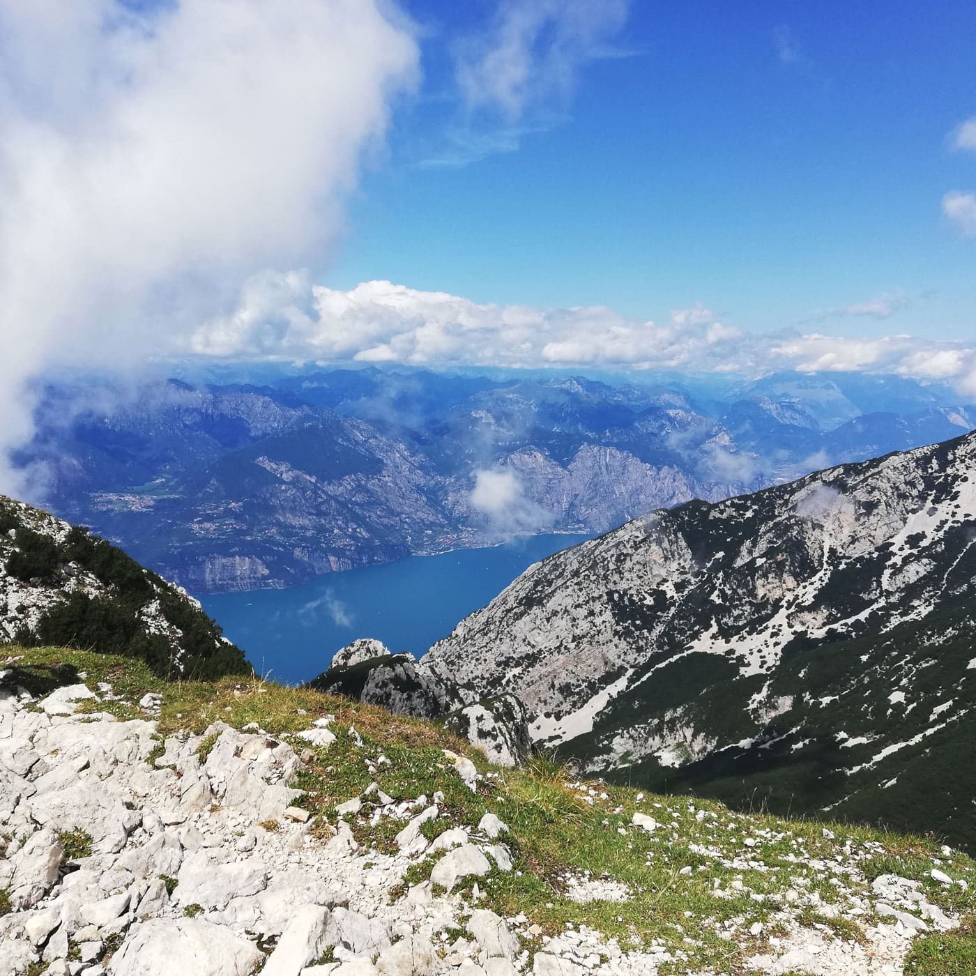 Bergaussichtspunkt mit felsigem Vordergrund, blauem See und fernen, schneebedeckten Gipfeln unter strahlend blauem Himmel