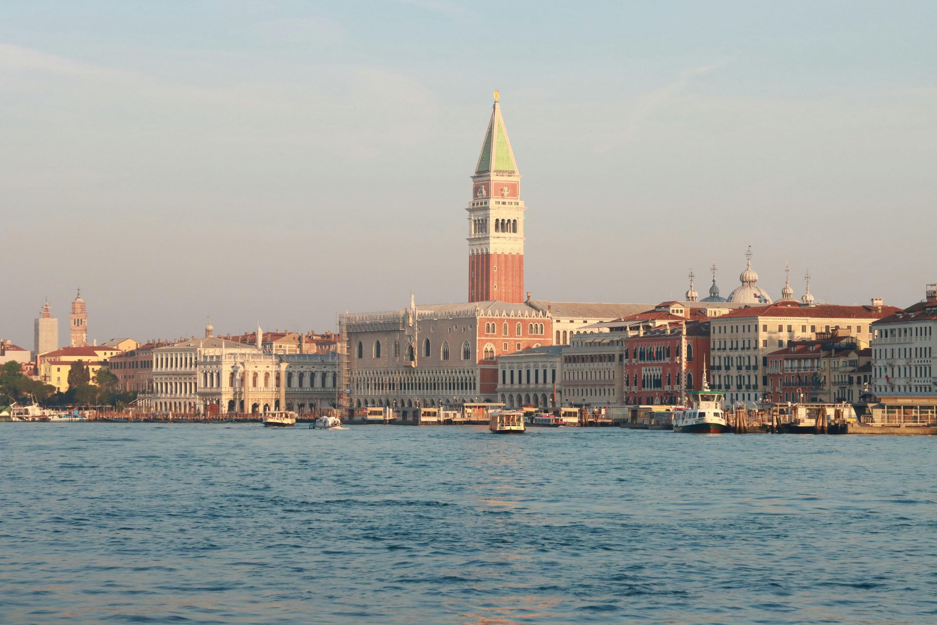 Il lungomare di Venezia con il Campanile di San Marco e gli edifici storici sull'altra sponda al tramonto.