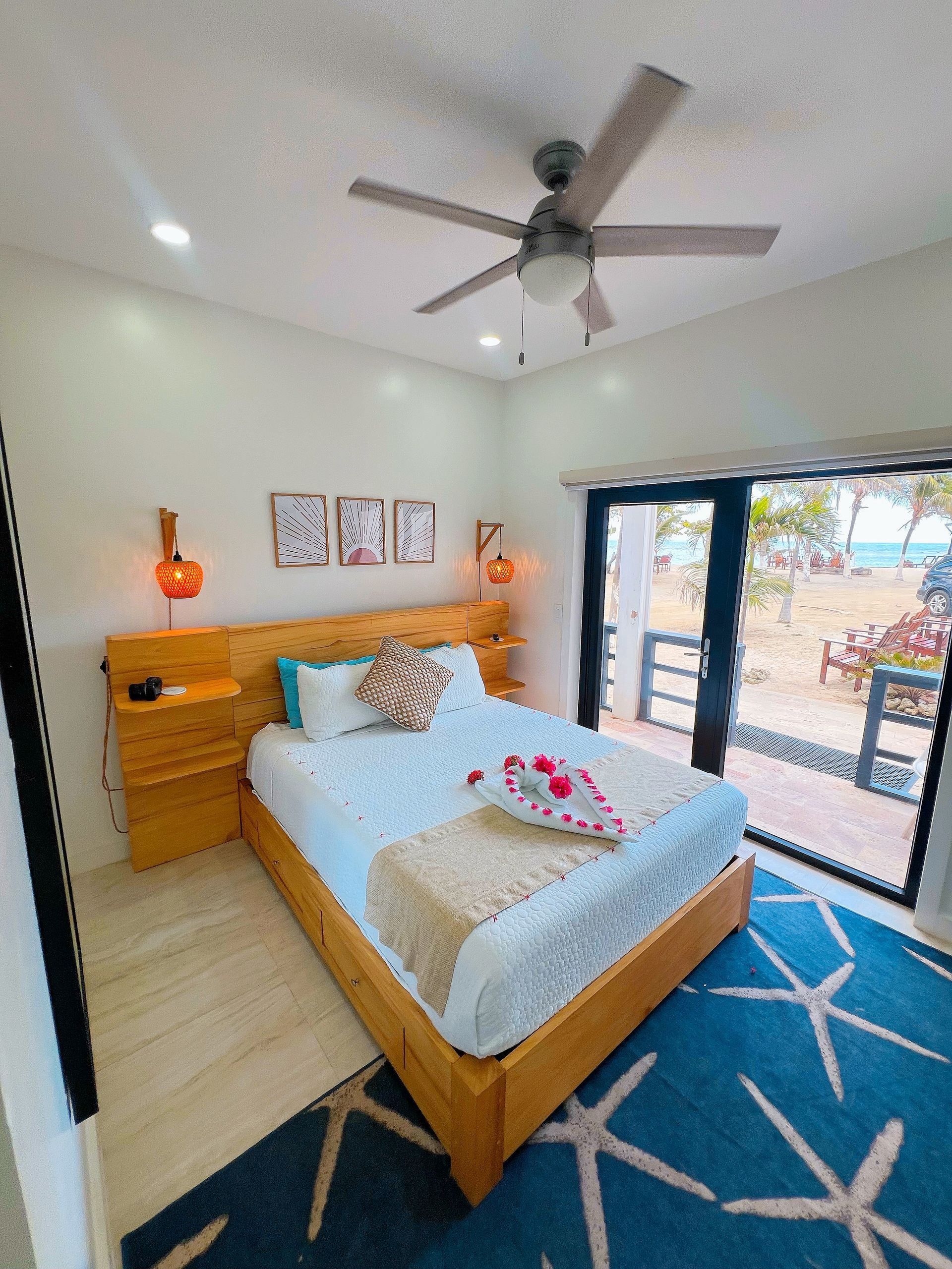 Bedroom with wooden bed, blue star rug, and view of beach through sliding glass door.