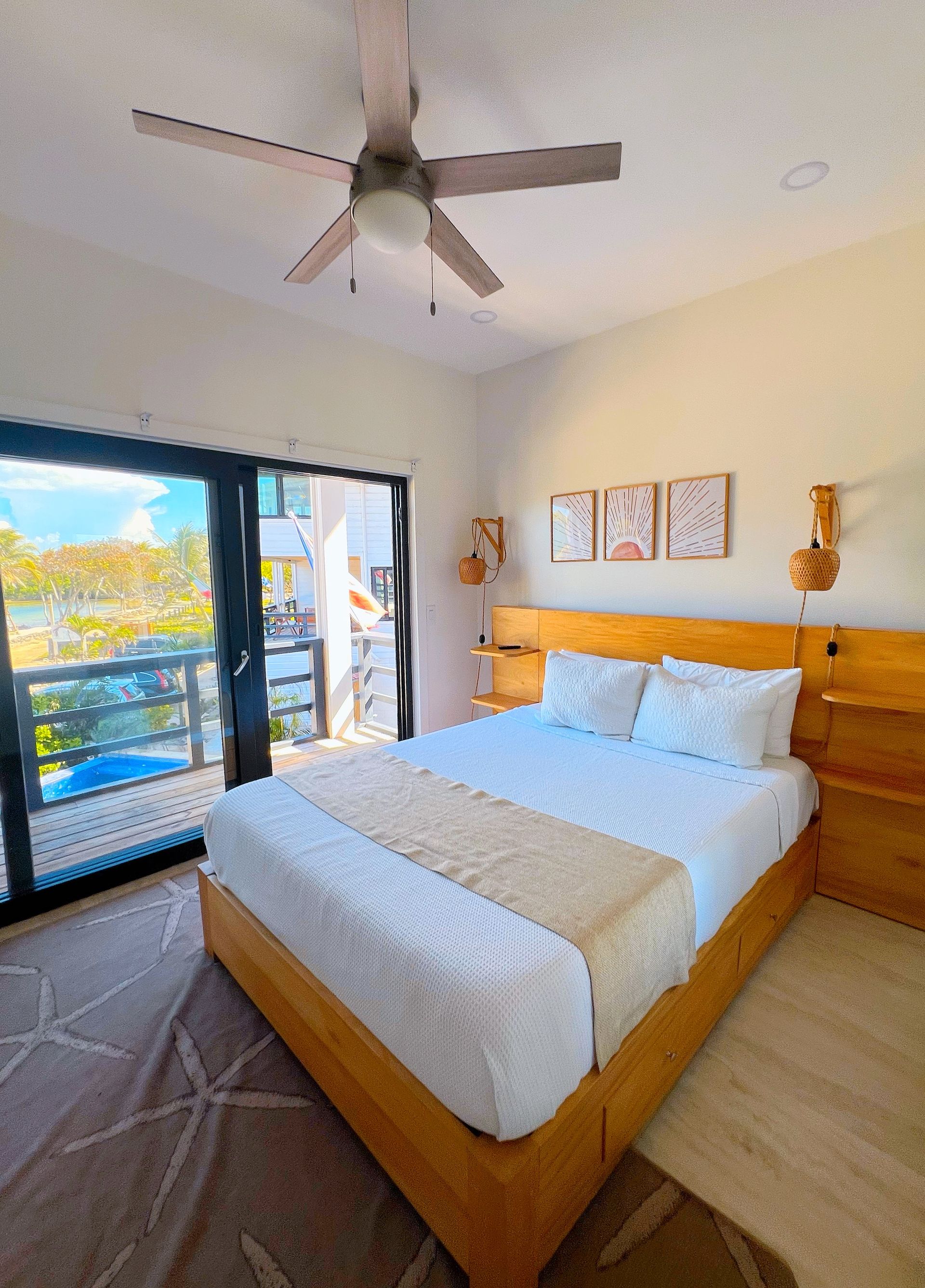 Bedroom with a wooden bed, sliding glass door to balcony, neutral tones, and ceiling fan.