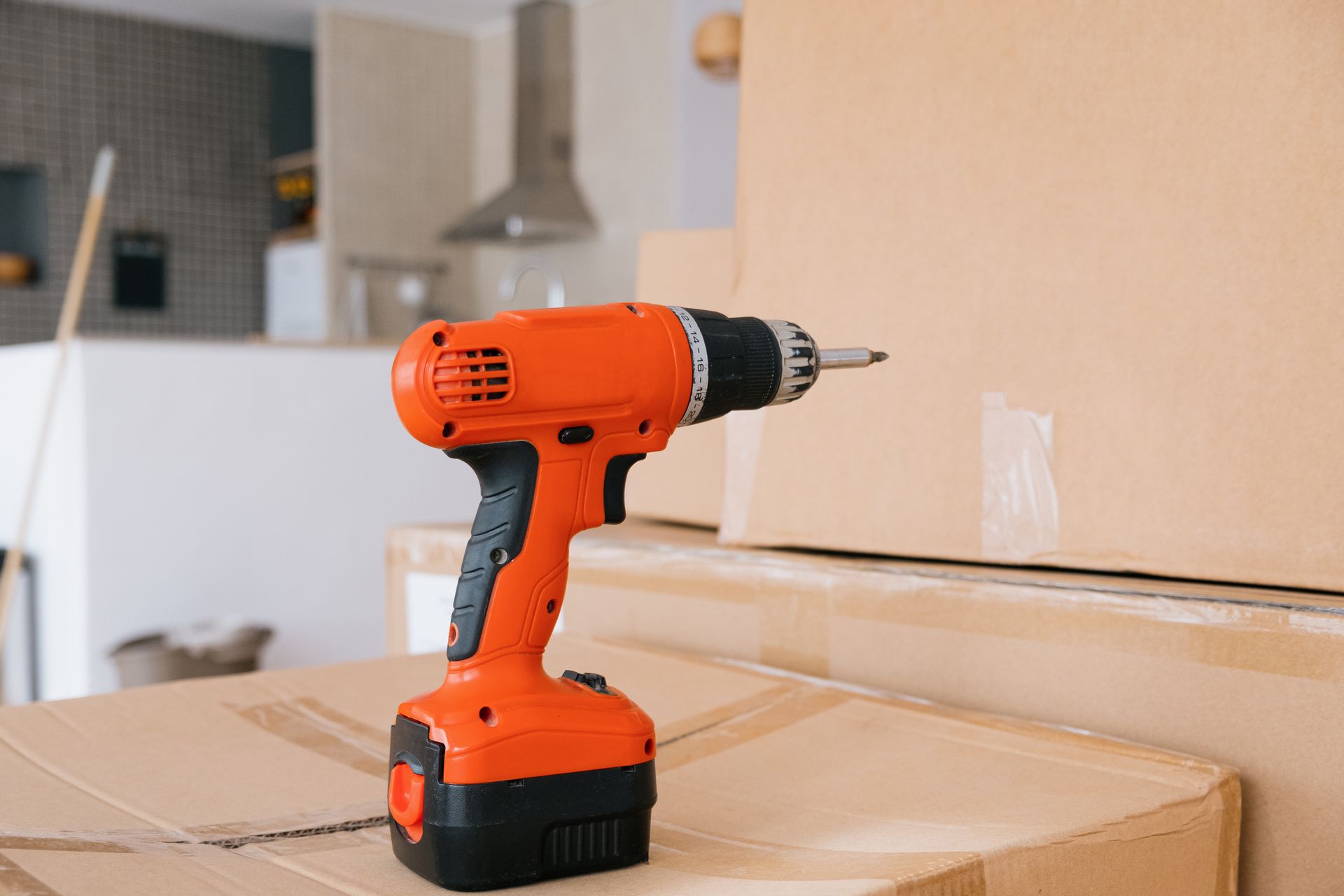 Orange cordless power drill on cardboard boxes during home renovation or moving.