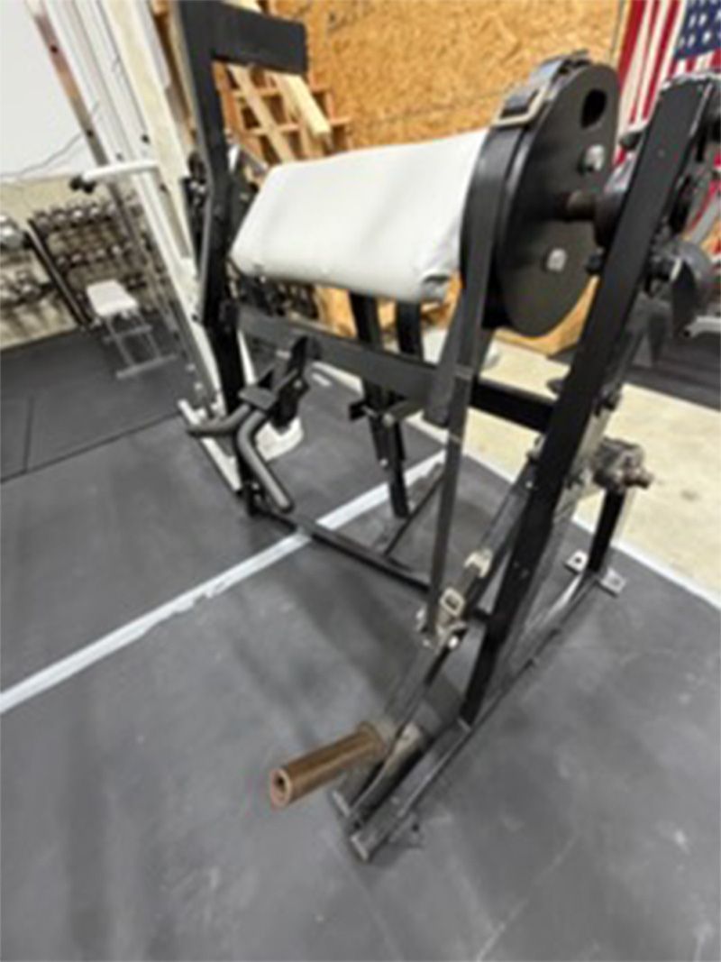 Leg press machine in a gym with a padded seat and metal frame on rubber flooring