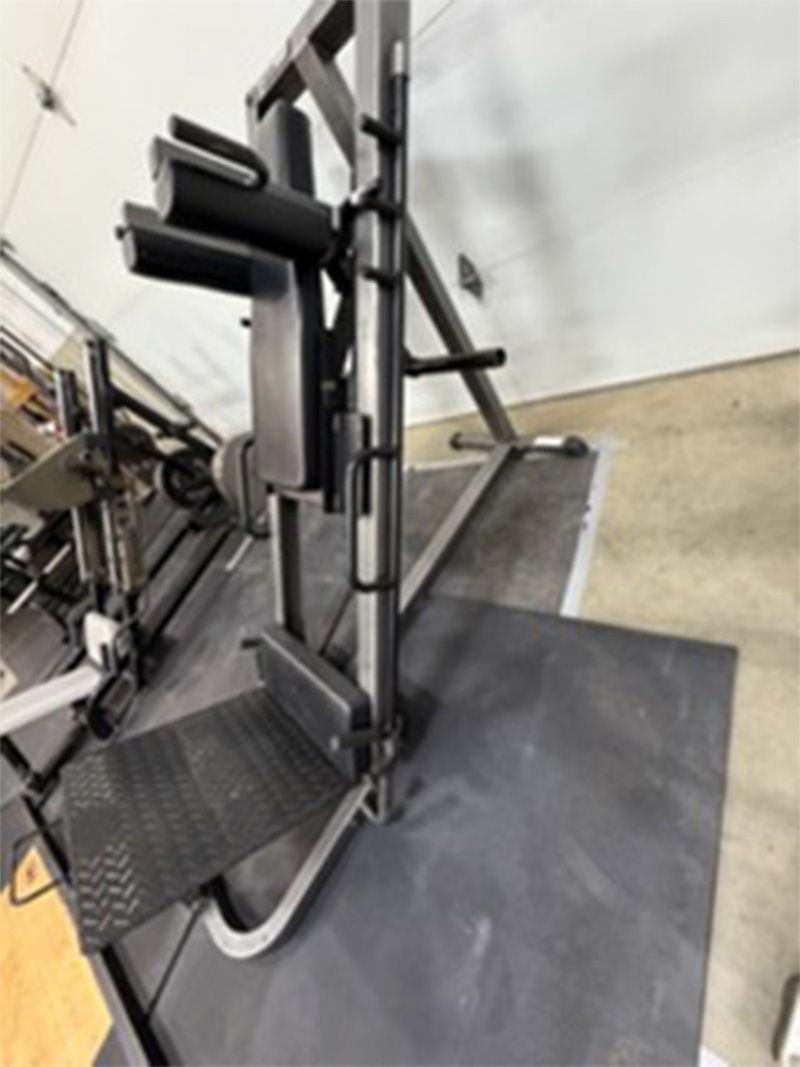 Gym strength machine with padded seat and footplate on a black mat in a fitness room