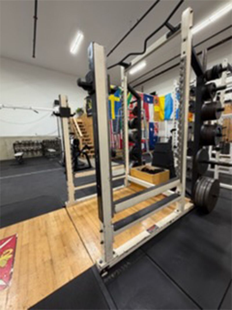 Gym squat rack on a wooden lifting platform with weight plates and resistance bands nearby