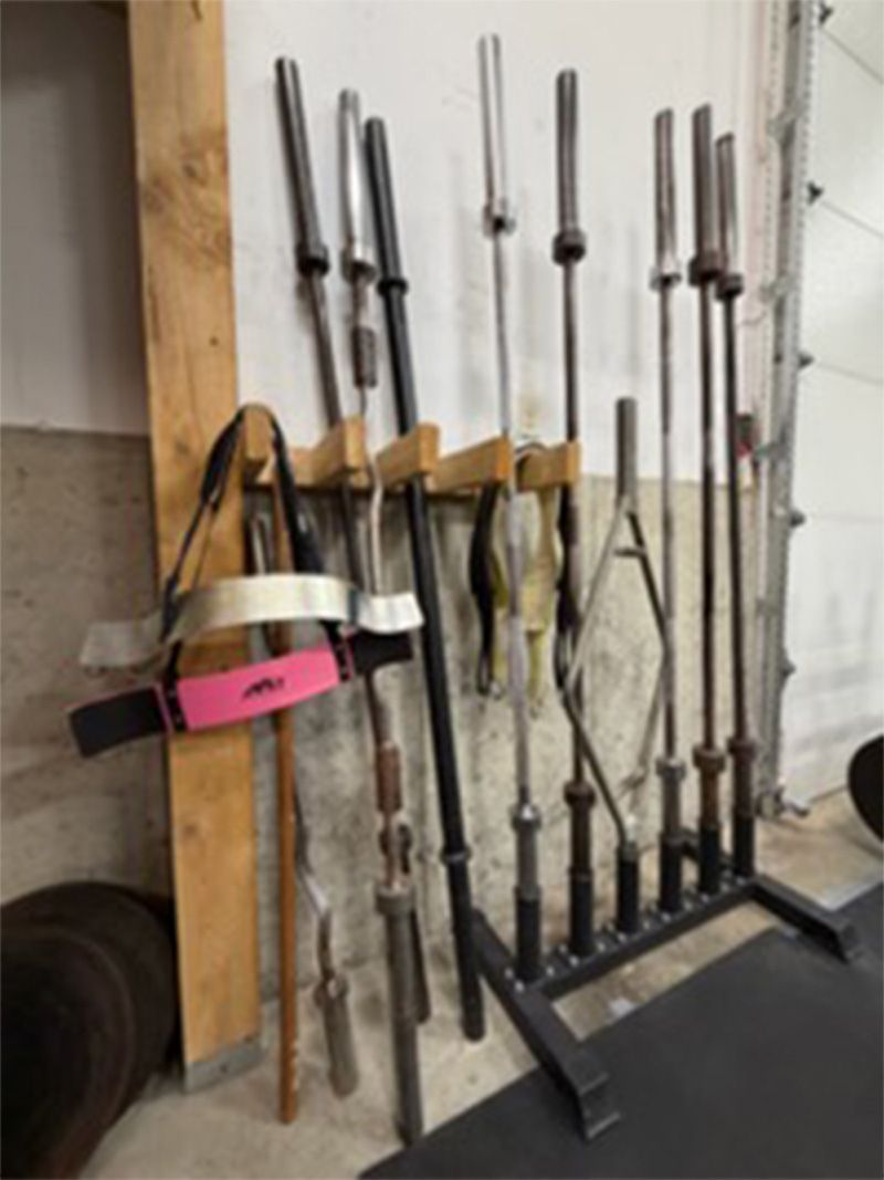 Assorted rifles and long guns leaning against a wall on a rack in a workshop or storage area