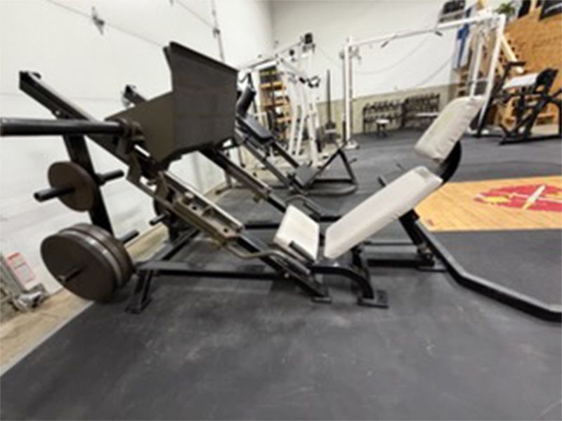 Leg press machine in a gym with white seat and black frame on rubber flooring