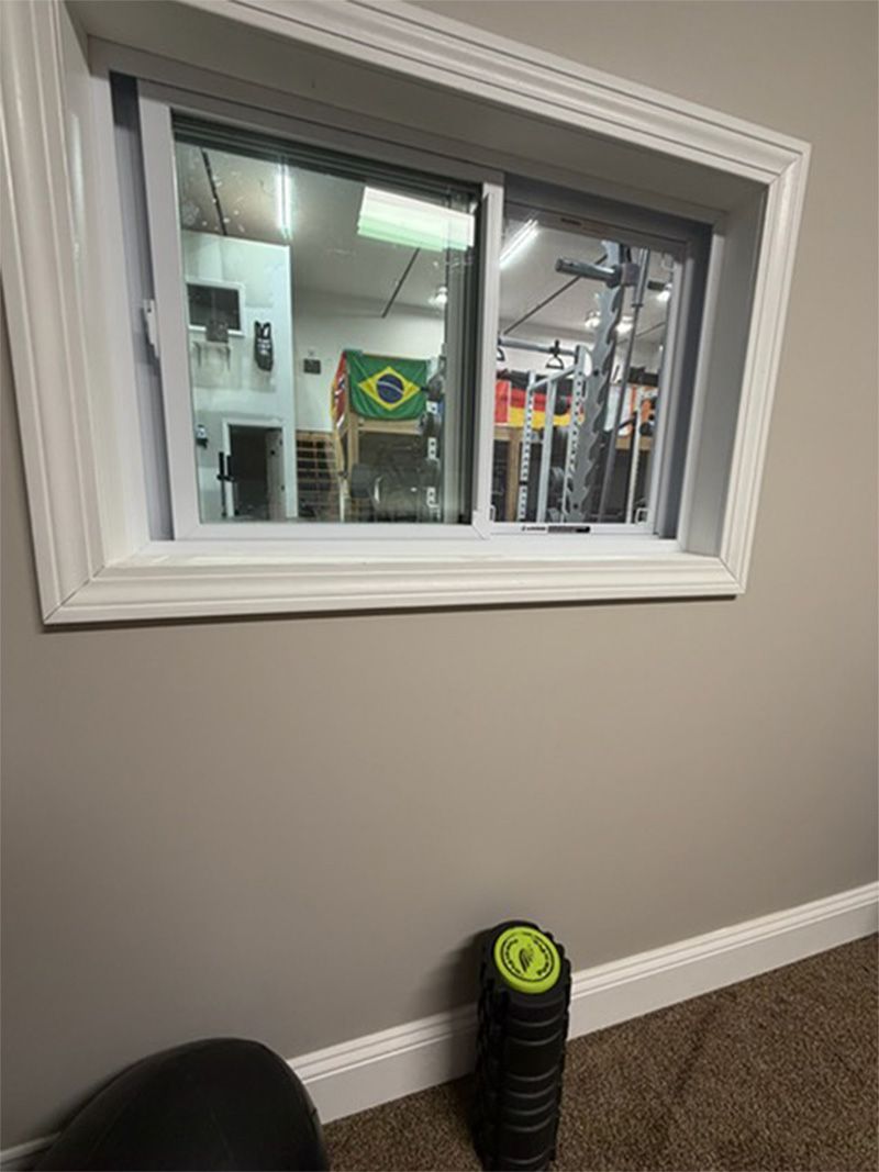 Gym interior seen through a wall window, with a green weight plate near the baseboard