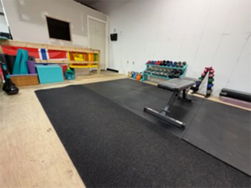 Indoor gym room with a rowing machine on dark mats and shelves of colorful equipment along the wall