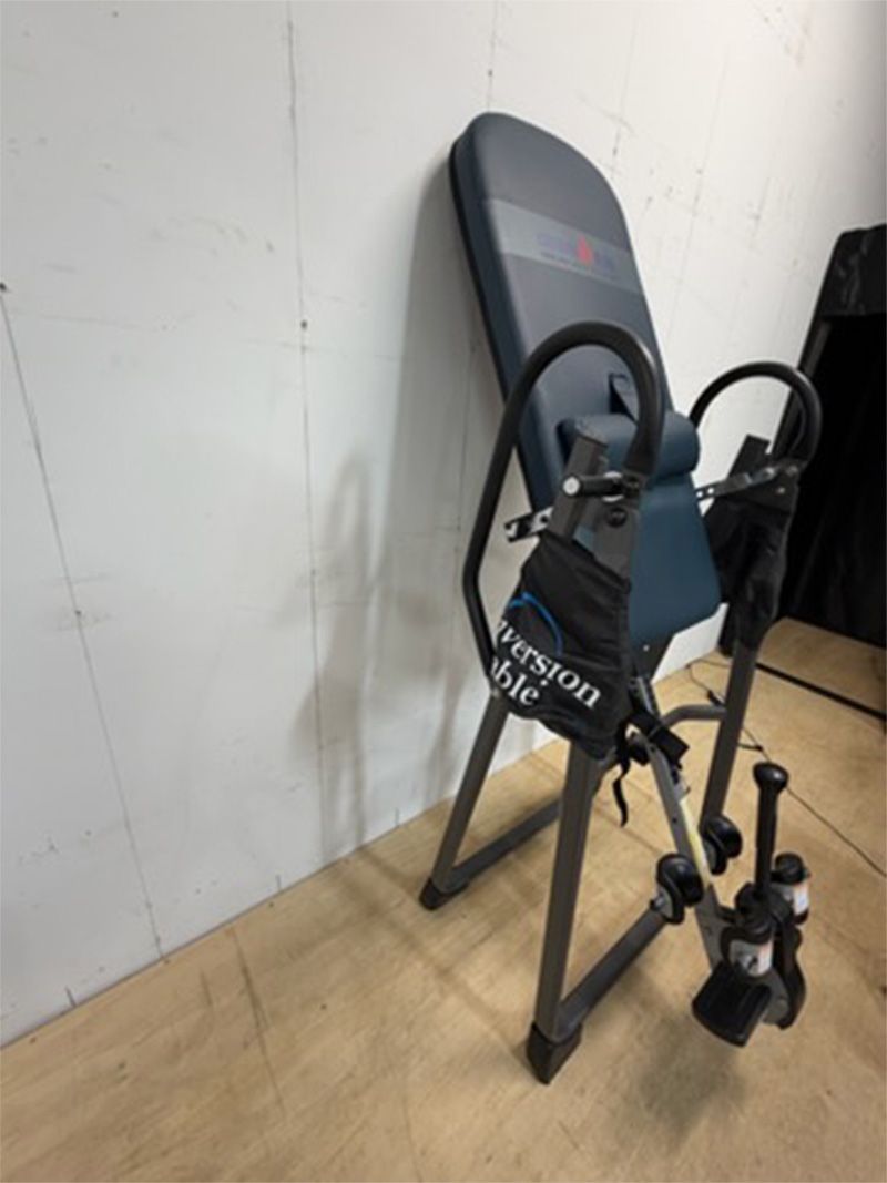 Ab workout bench with resistance handles leaning against a white wall in a gym room