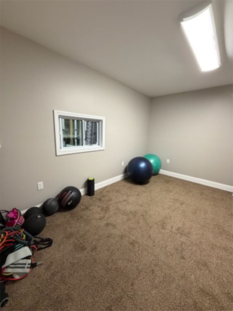 Empty beige room with carpet, small window, and exercise balls along the wall
