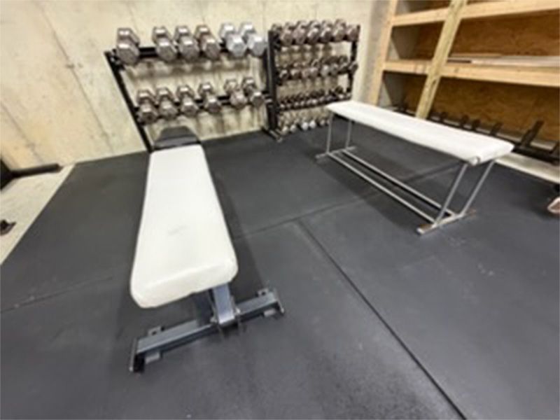 Gym interior with two white benches and a dumbbell rack against the wall