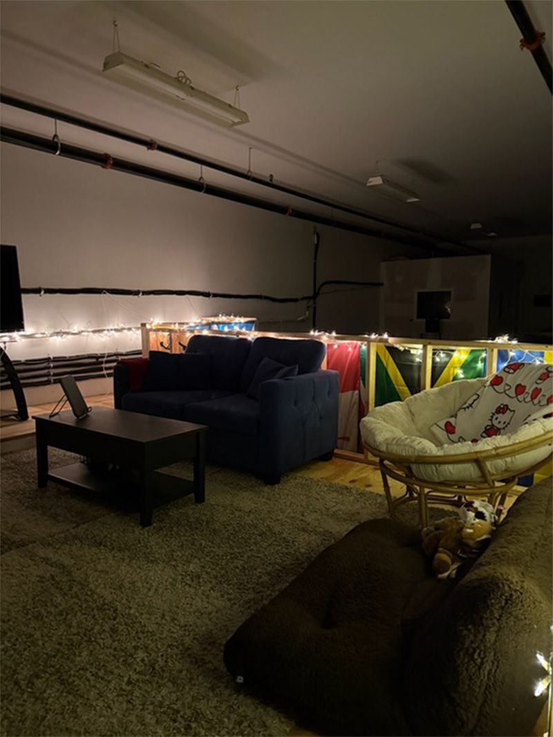 Dim lounge area with blue couch, coffee table, hanging chair, and string lights in a dark room