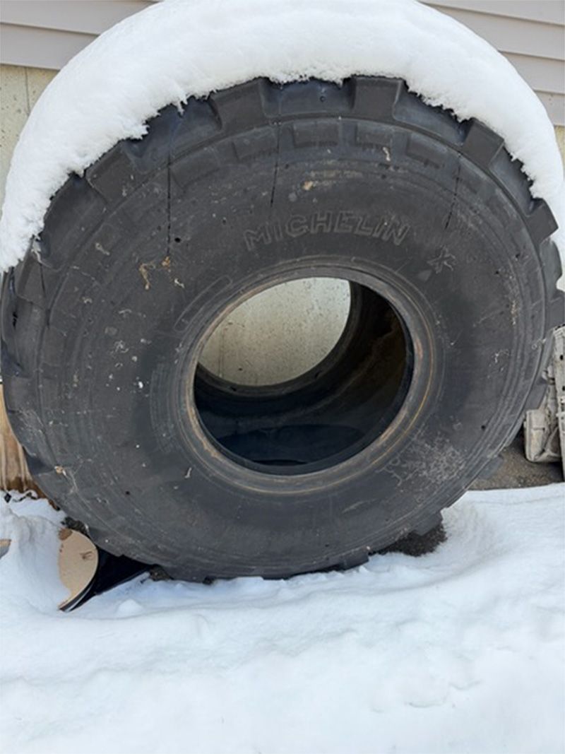 Large black tire partially covered in snow, standing outdoors on a snowy ground.