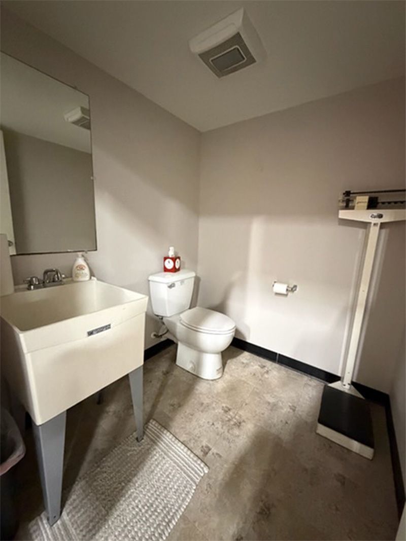 Small beige bathroom with sink, toilet, mirror cabinet, towel rug, and trash bin