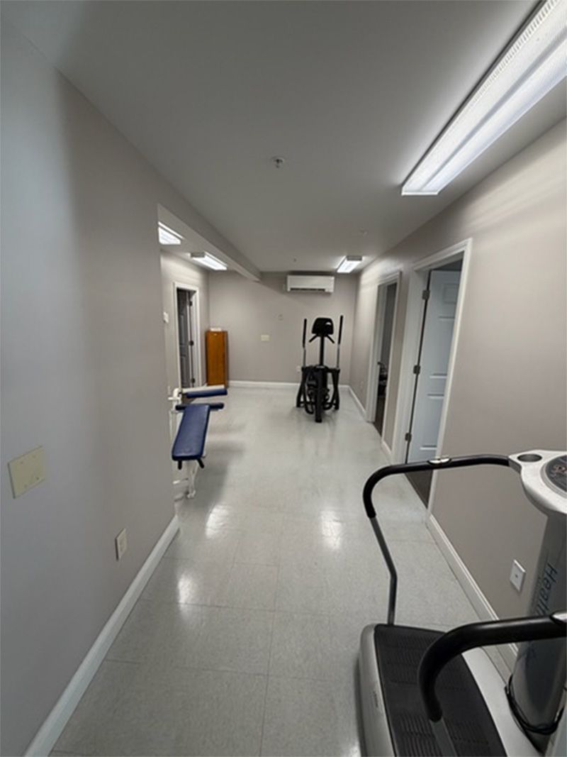 Narrow hospital corridor with bright overhead lights, medical equipment, and a wheelchair in the foreground