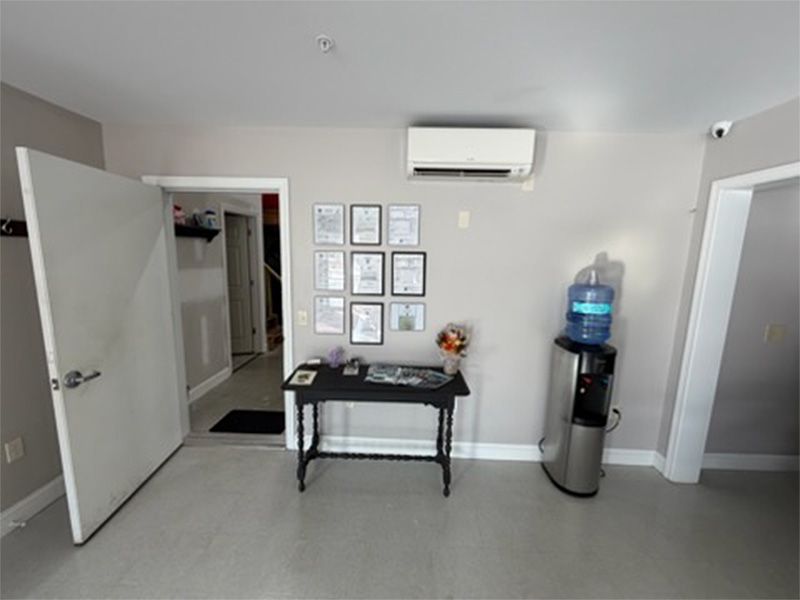 Small office lobby with framed wall art, black table, water cooler, and open door to hallway.