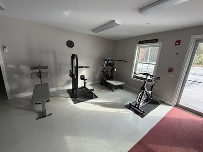 Small home gym with exercise machines, white walls, and a red carpeted area near a window and door