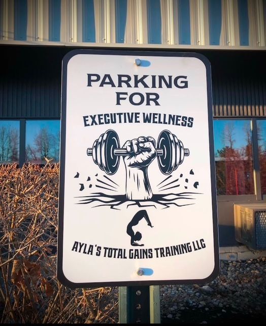 Sign: Parking for Executive Wellness; logo of a weightlifting arm above a person in a yoga pose. Ayla's Total Gains Training LLC.